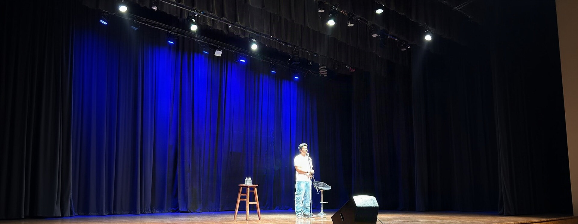 Stand-up comedian mid-set on a blue-lit theatre stage at a Show Company comedy night